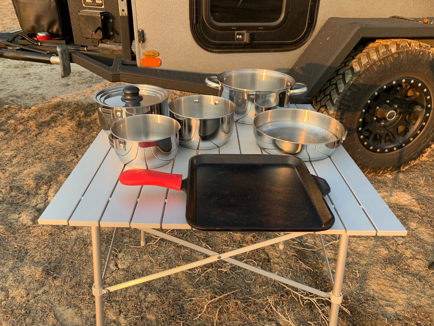 Essential camping cooking gear: pots, pans, and a griddle on a table, perfect for your RV rental outdoor kitchen.