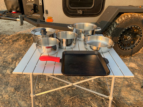 Essential camping cooking gear: pots, pans, and a griddle on a table, perfect for your RV rental outdoor kitchen.