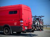 Red Sprinter van, an RV rental, with two bicycles on a rear rack. Ready for travel and outdoor adventures by the coast.