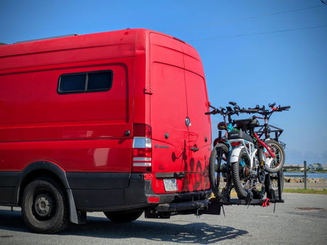 Red Sprinter van, an RV rental, with two bicycles on a rear rack. Ready for travel and outdoor adventures by the coast.