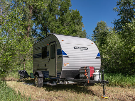 This compact Sunray Sport RV rental is ready for adventure, nestled in a grassy, tree-lined campsite. Perfect for outdoor escapes.