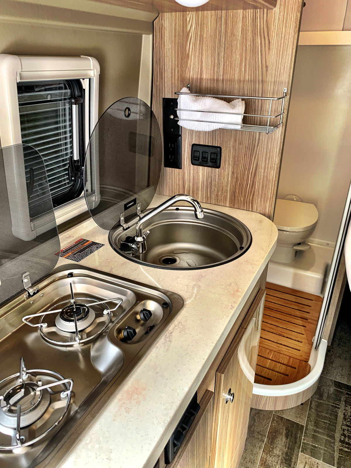 Inside an RV rental: functional kitchen area with a stove & sink, plus a compact wet bath including a toilet and shower. — photo 6