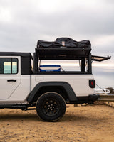 White Jeep Gladiator pickup with truck bed cap, rooftop tent, and cooler, ideal for your next RV rental overlanding trip.