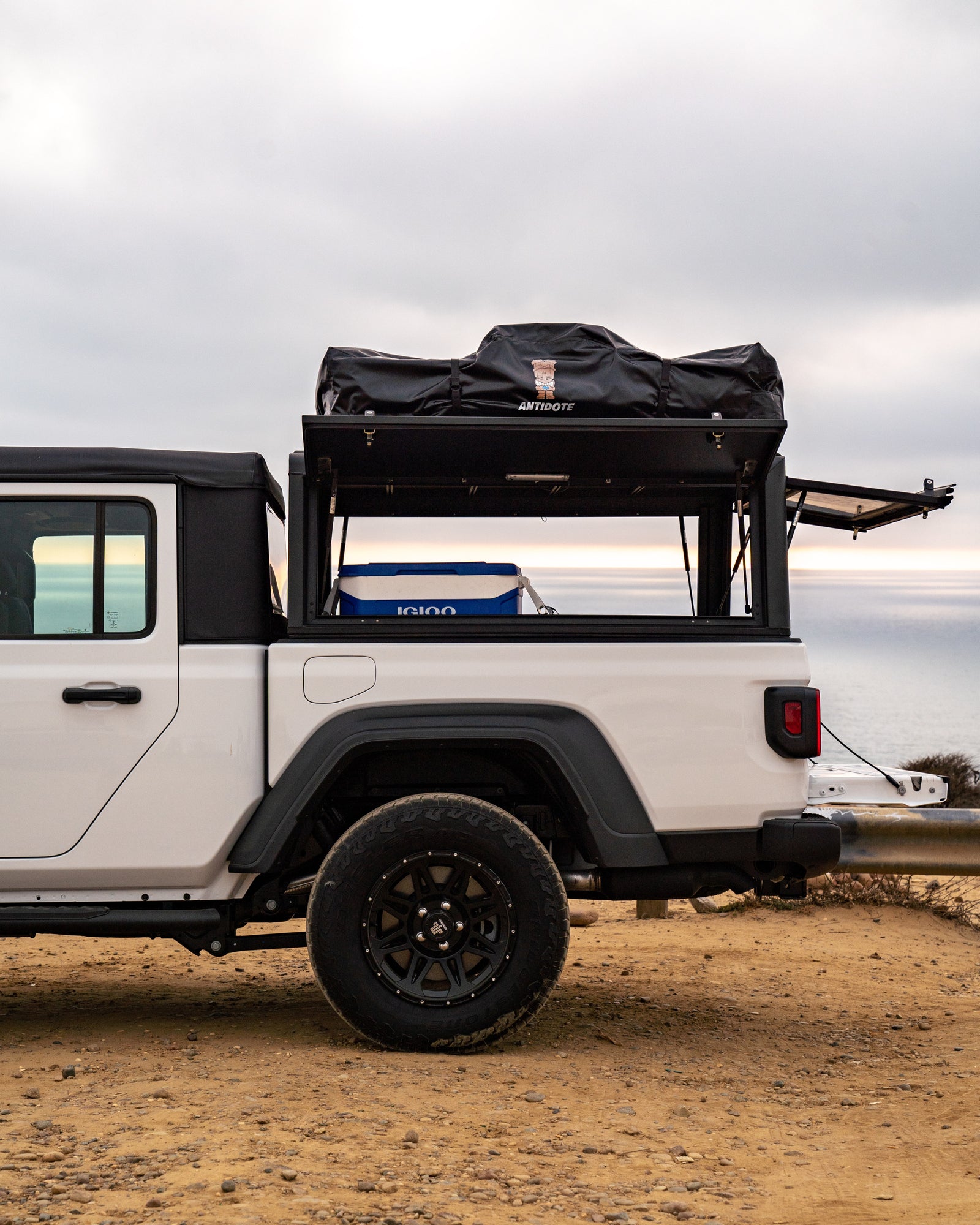 White Jeep Gladiator pickup with truck bed cap, rooftop tent, and cooler, ideal for your next RV rental overlanding trip.