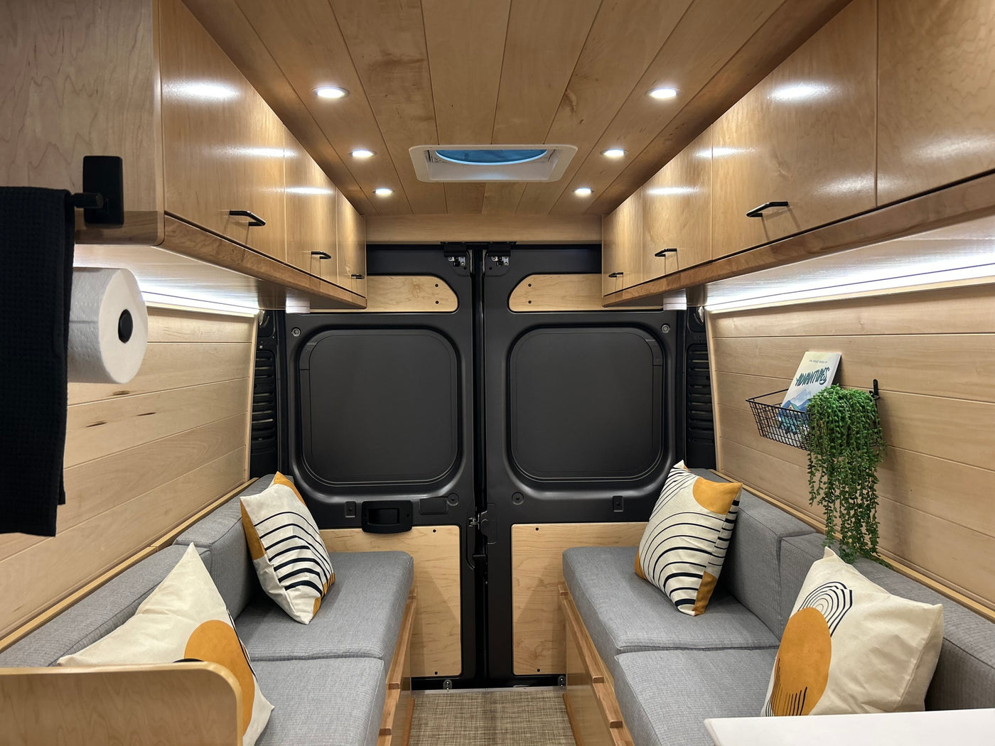 Cozy, modern camper van interior for your next RV rental adventure, featuring warm wood, comfy seating & smart storage. — photo 2