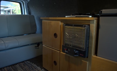 RV rental interior: custom wood cabinetry with an integrated heater, stove, and fridge, plus a comfy grey bench seat. — photo 8