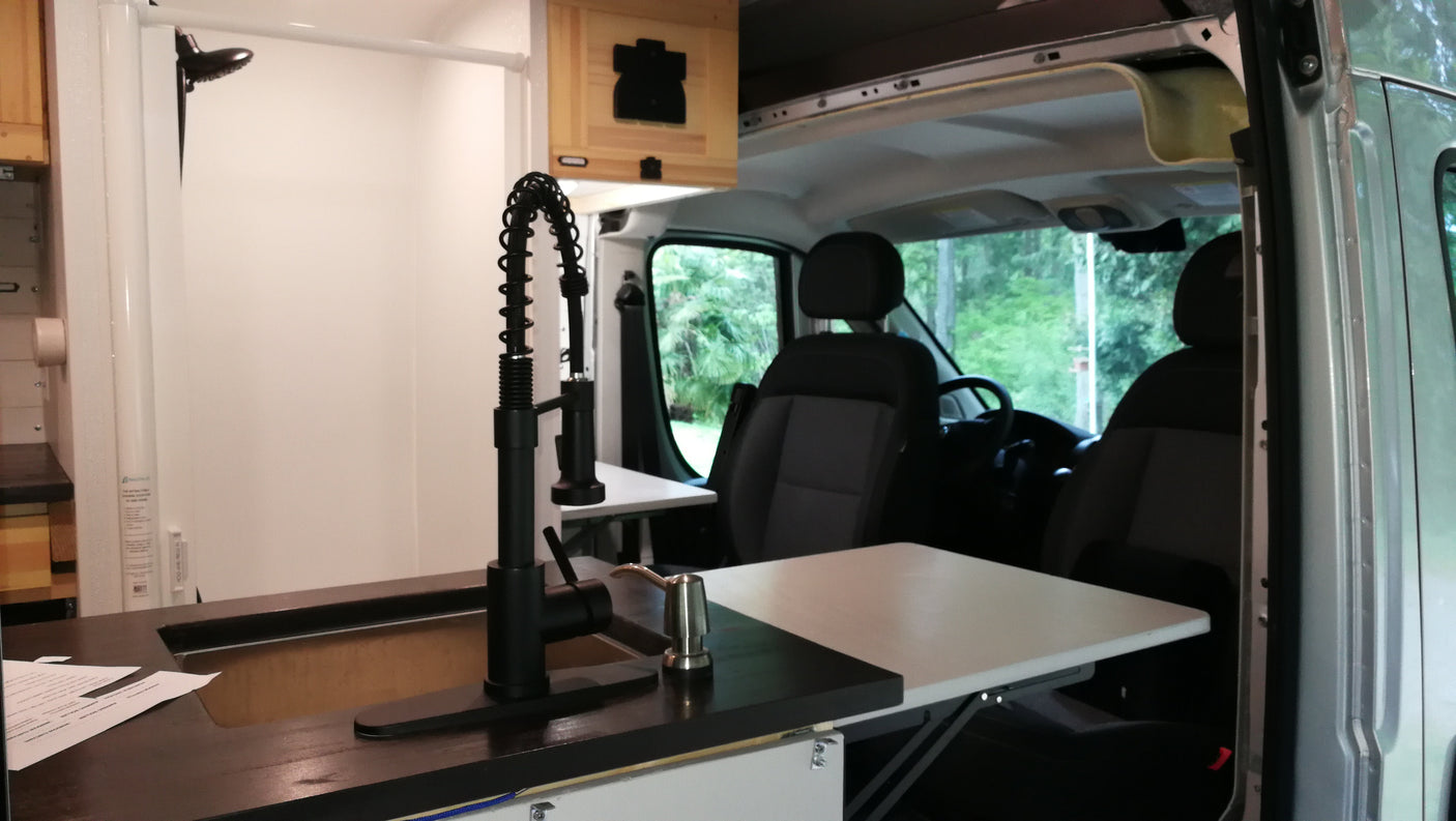 RV rental: Modern camper van interior with kitchen, extendable table, black faucet, and a shower for comfortable travel.