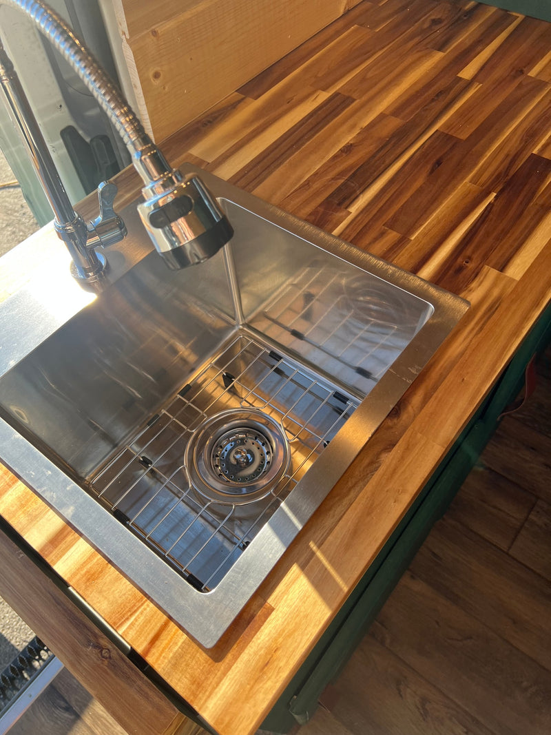 Modern RV rental kitchen featuring a stainless steel sink with grid, pull-down faucet, and warm wood countertop. — photo 11