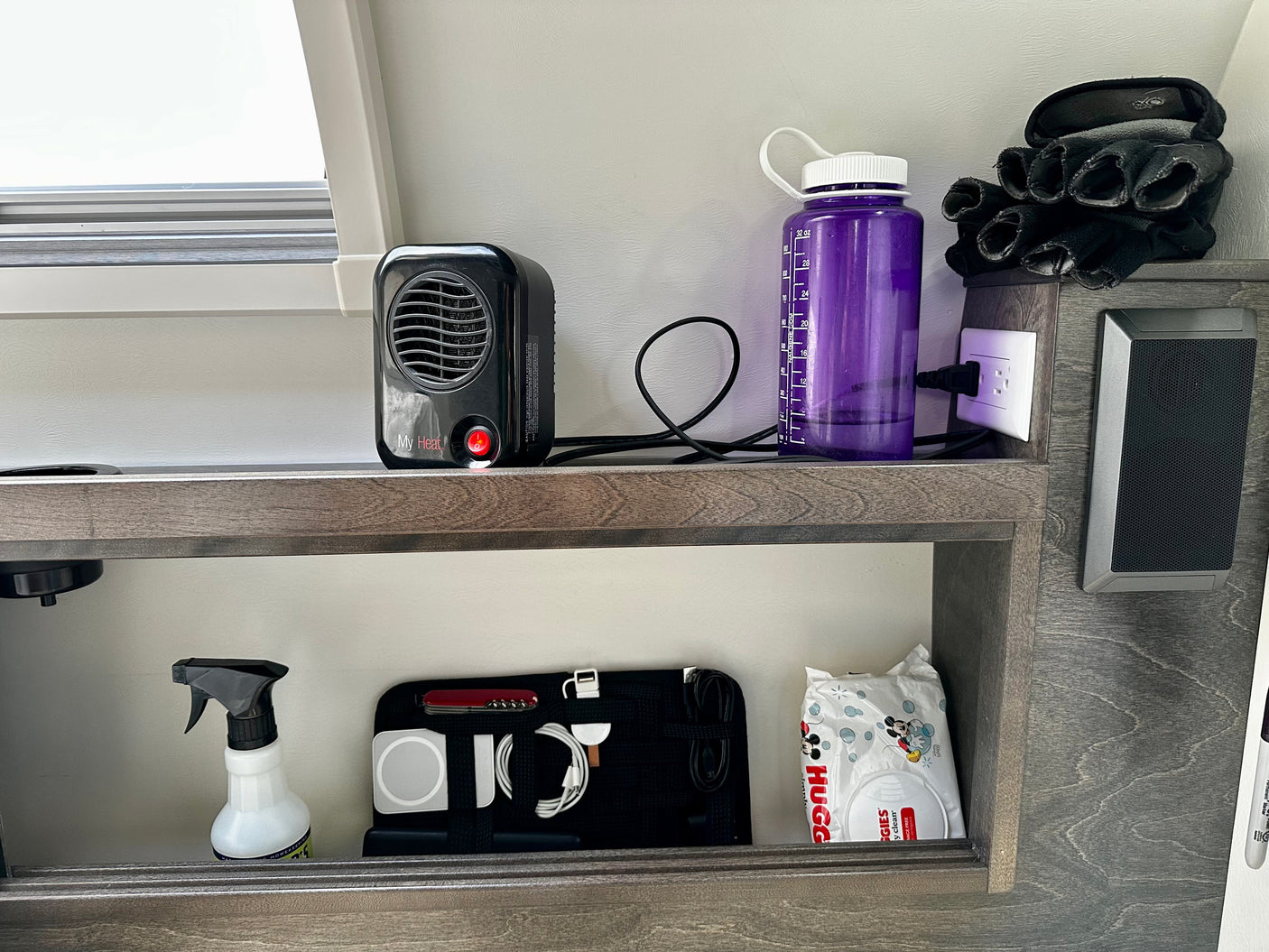 Organized shelving inside an RV rental, with a personal heater, water bottle, tech essentials, and wipes for convenience.