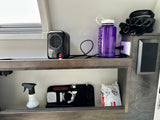 Organized shelving inside an RV rental, with a personal heater, water bottle, tech essentials, and wipes for convenience.