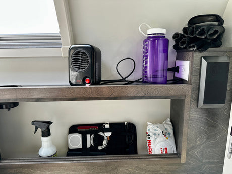 Organized shelving inside an RV rental, with a personal heater, water bottle, tech essentials, and wipes for convenience.