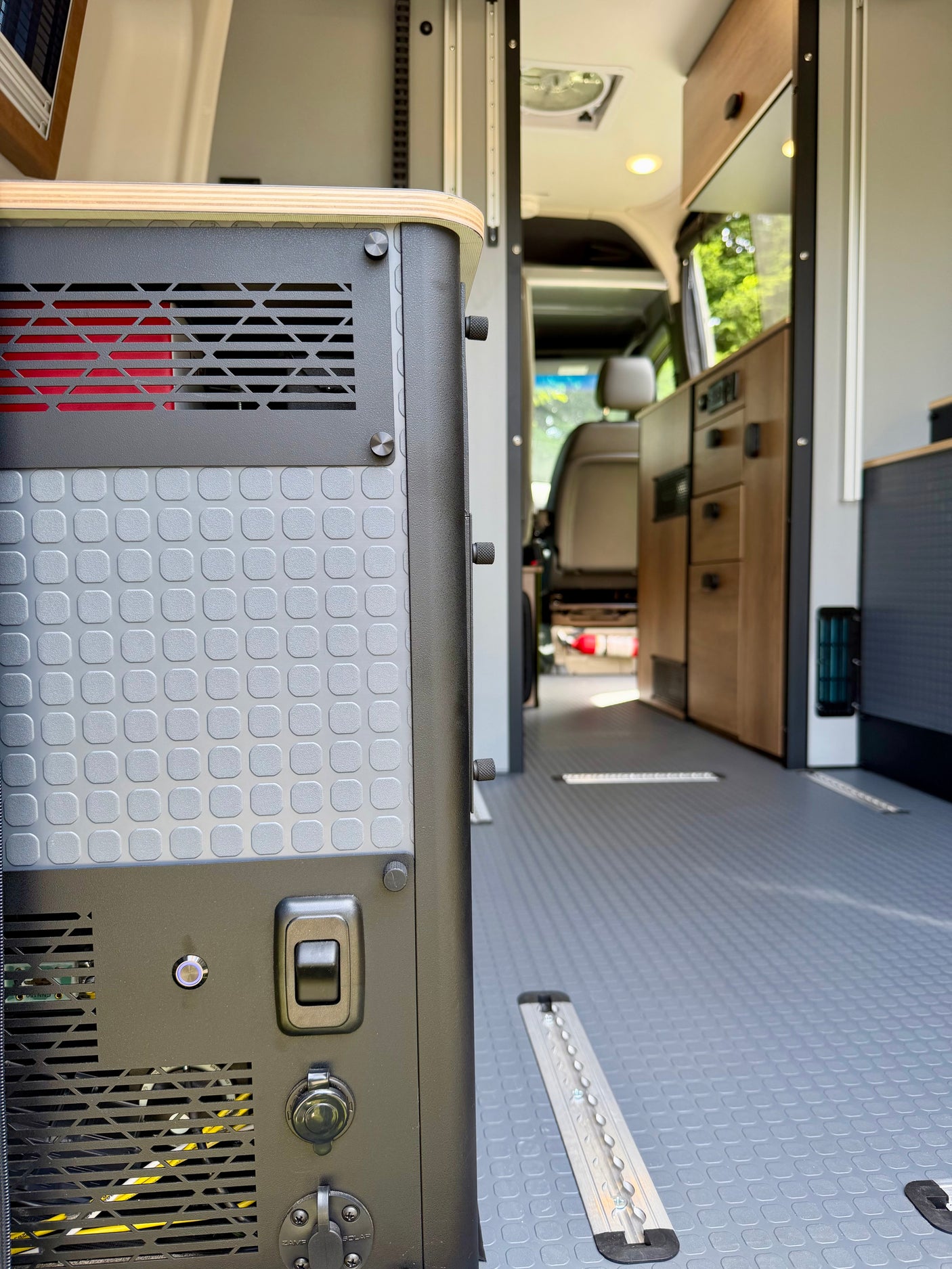 RV rental interior: Focus on a power station with textured panels, vents, and charging ports, set against the clean van floor and cabinetry.