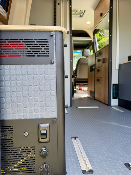 RV rental interior: Focus on a power station with textured panels, vents, and charging ports, set against the clean van floor and cabinetry.