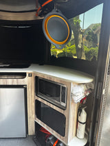 Inside RV rental: compact kitchen with microwave, fridge, cooktop, and hanging collapsible bowl. Fire extinguisher visible.