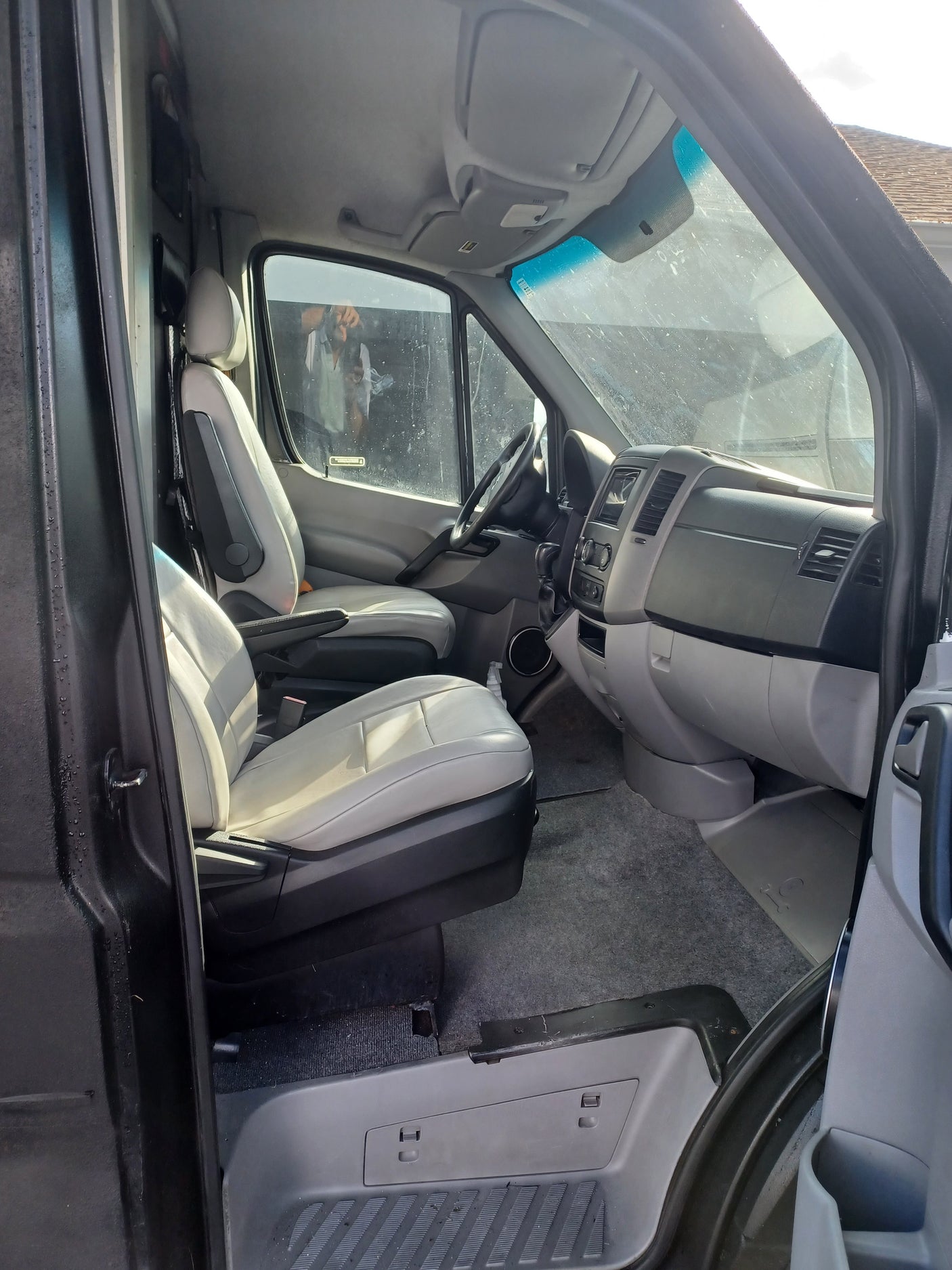 Angled view of an RV rental's cab interior: light gray driver & passenger seats, dashboard, and steering wheel are visible.