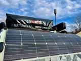 An RV rental setup: roof-mounted solar panel, packed 23ZERO rooftop tent, and a tall antenna under a blue sky.