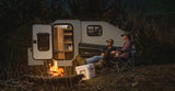 Two people relaxing by a cozy campfire next to a compact camper under a starry sky, perfect for an RV rental getaway.