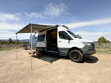 RV rental camper van with extended awning & open door on dirt road, ready for adventure in an open landscape.