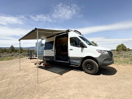 RV rental camper van with extended awning & open door on dirt road, ready for adventure in an open landscape.