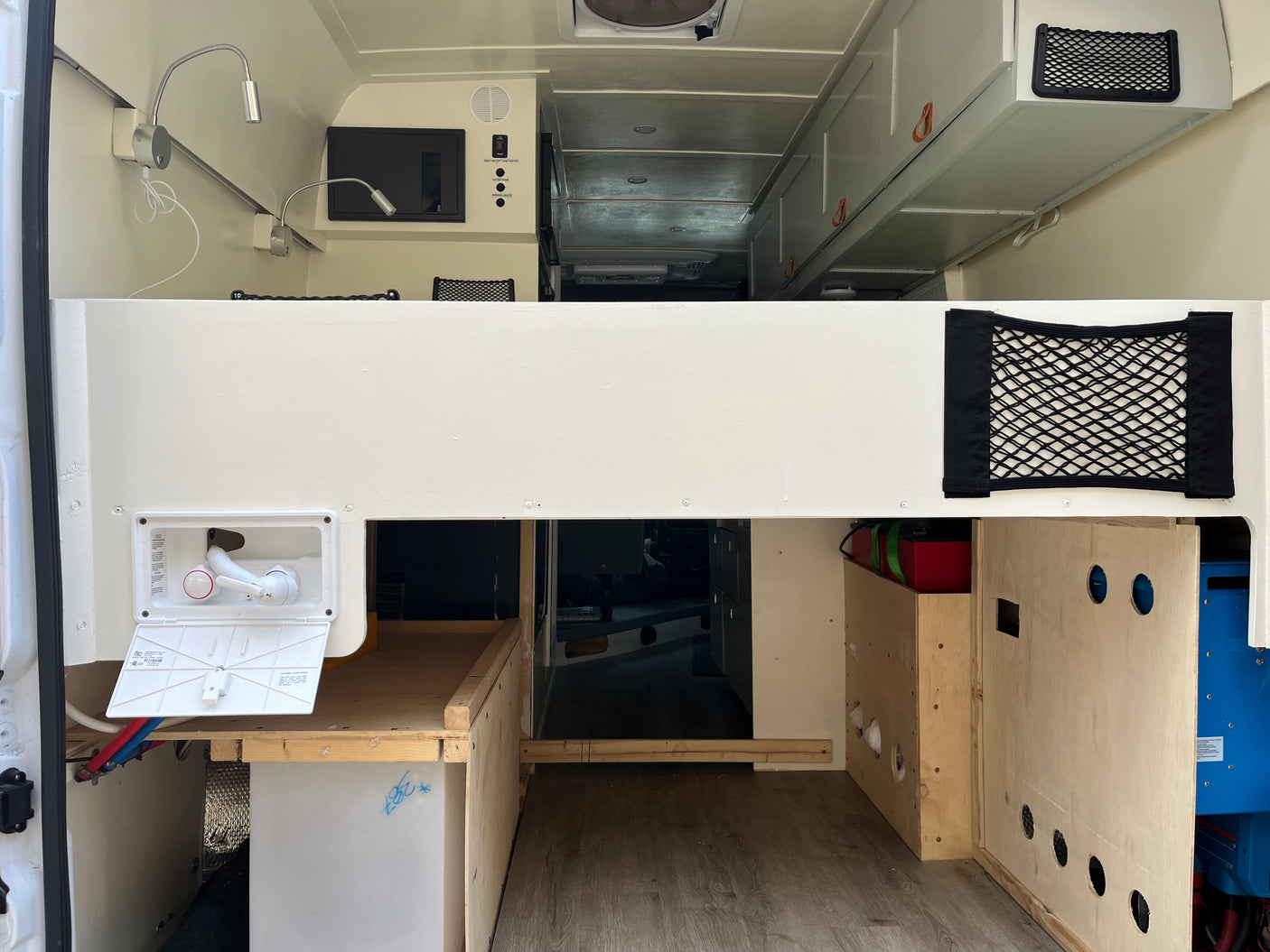 This RV rental shows a camper van interior with an elevated bed, lights, controls, shower, and storage solutions.