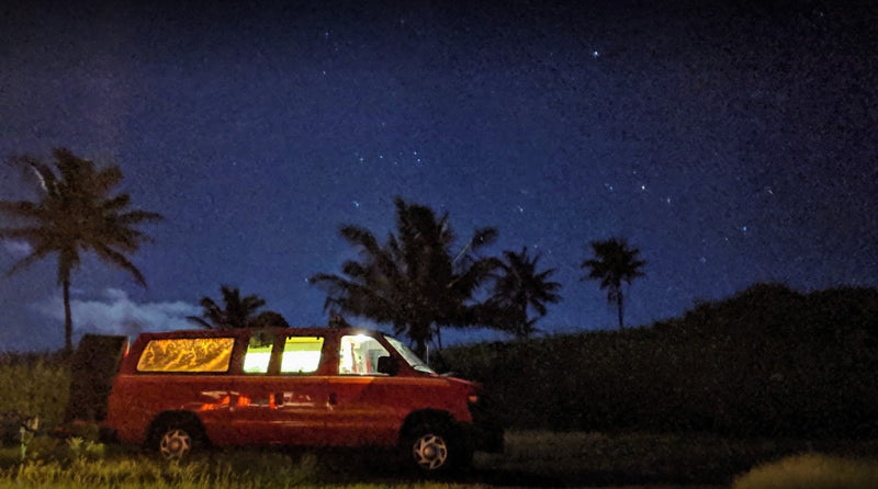 A red rv rental van with lit interior, parked under a clear night sky filled with stars, surrounded by palm trees. — photo 14