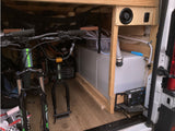 RV rental interior: organized bike storage (mountain, BMX) alongside a van conversion's fresh water tank and pump system.