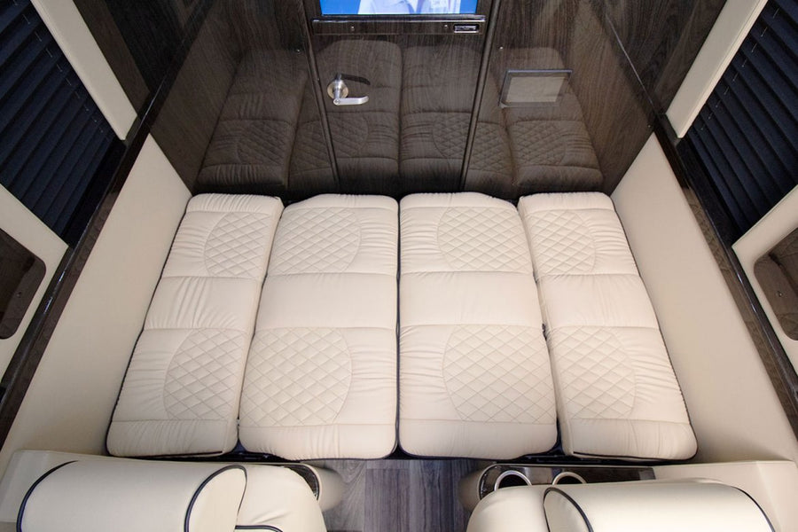 Luxury RV rental interior with comfortable quilted bedding laid out, converting from seating for a spacious sleeping area.