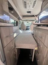 RV rental interior: Cozy camper van with convertible bed, wood-grain cabinets, and a view to the front cab.