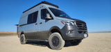 A light blue Mercedes Sprinter REVEL 4x4 camper van for RV rental, parked off-road in a desert landscape.