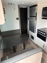 Inside a modern rv rental: dinette, full kitchen with fridge, microwave, oven, and stylish wood-look flooring.