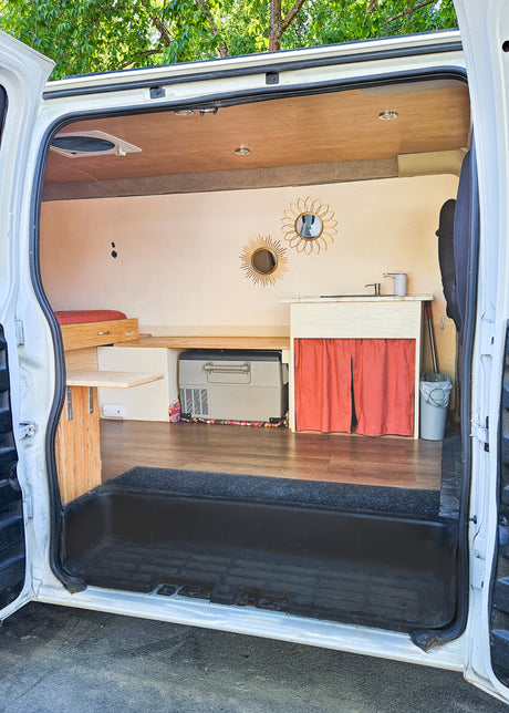 Cozy RV rental interior shows a clever camper van conversion with a kitchen, bed, and storage. Ideal for travel.