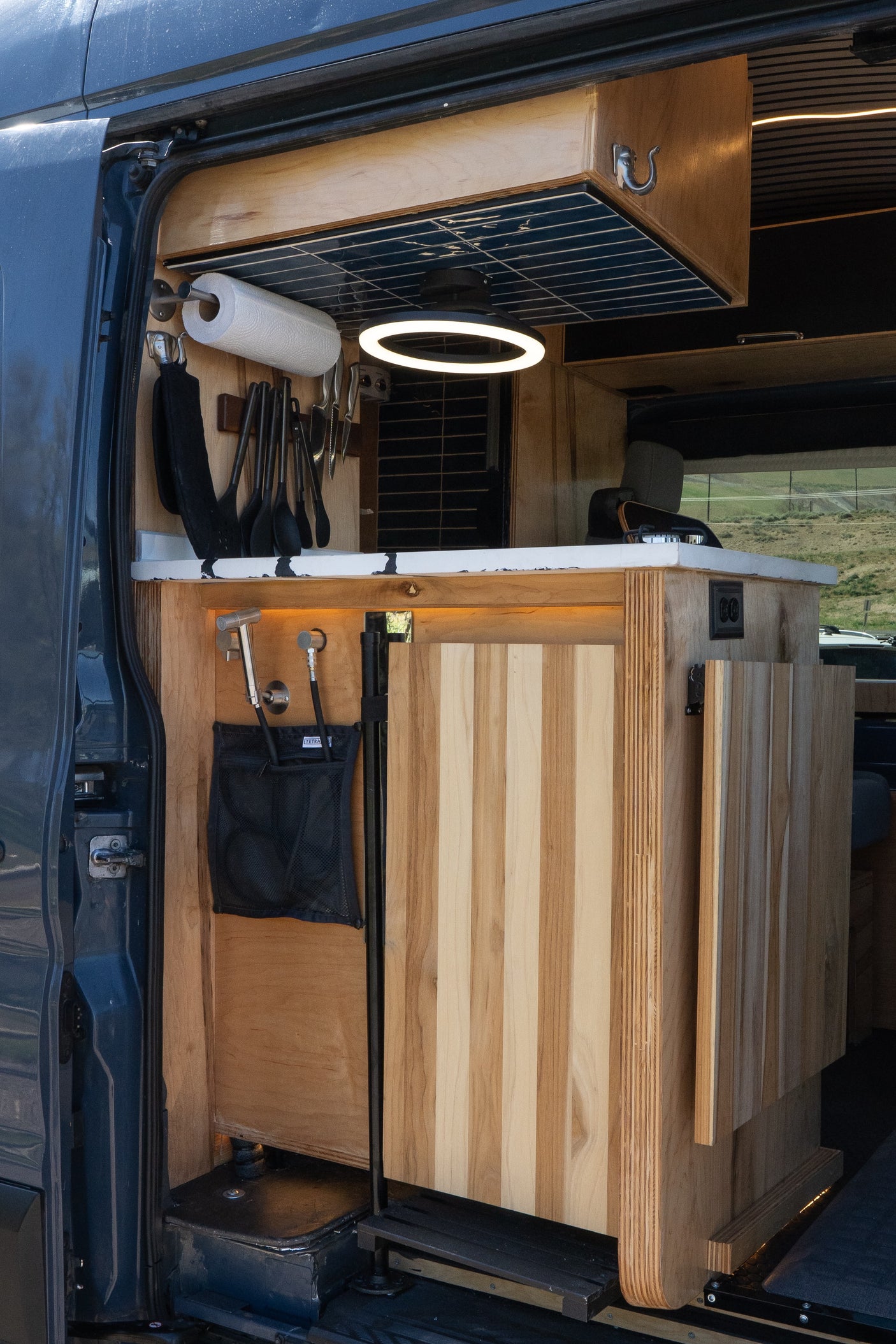 This RV rental's custom kitchen boasts wooden cabinetry, a sleek countertop, ring light, and clever utensil storage.