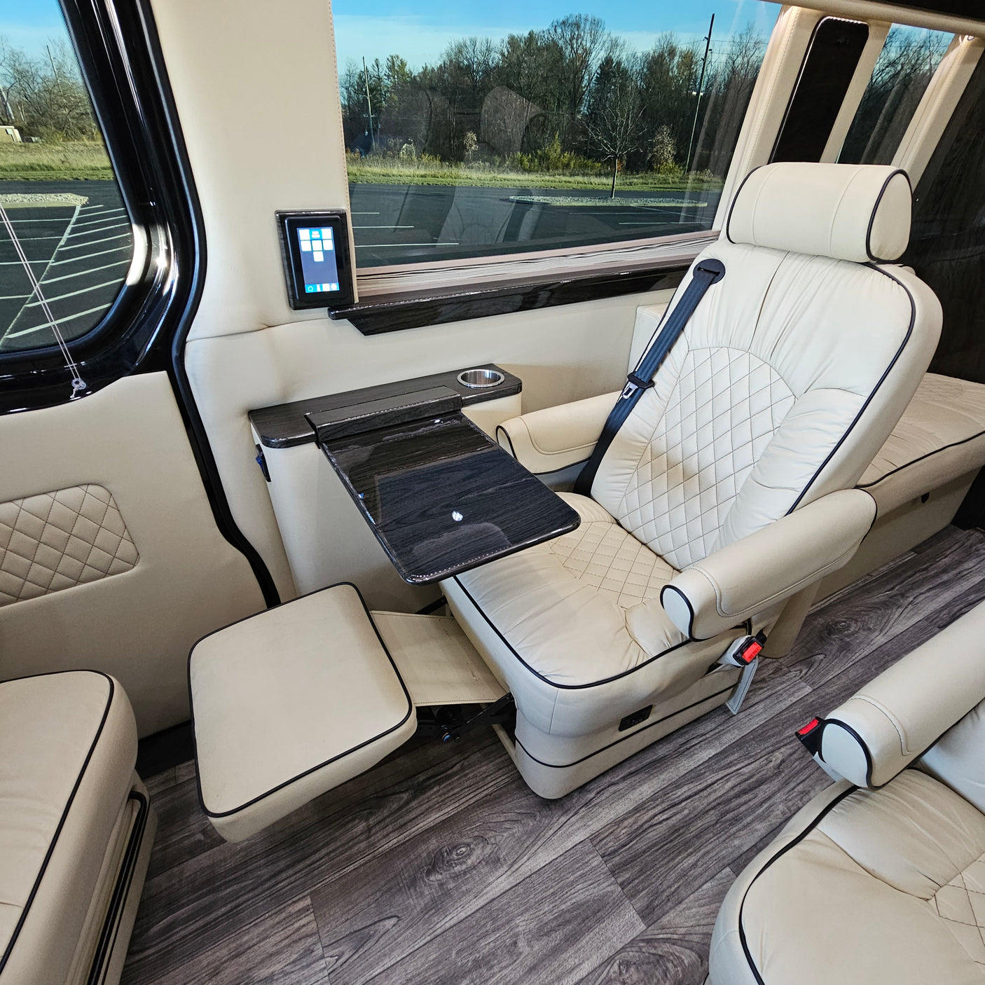 Inside a premium RV rental: cream leather captain's chair with footrest, work table, and wood-look flooring.
