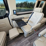 Inside a premium RV rental: cream leather captain's chair with footrest, work table, and wood-look flooring.