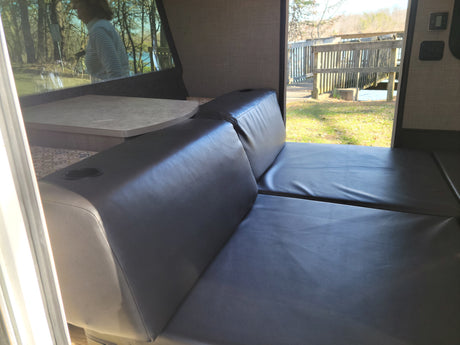 This RV rental interior features a convertible leatherette sofa/bed and dinette, with serene outdoor views.