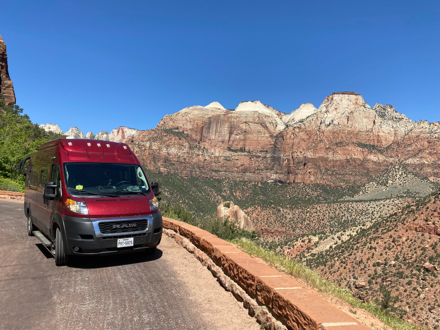 Red camper van rental on a scenic road overlooking majestic sandstone mountains, ideal for national park adventures.