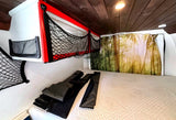 Cozy rv rental bed area with storage nets, wooden ceiling, and nature-themed curtain. Folded items rest on the bed.
