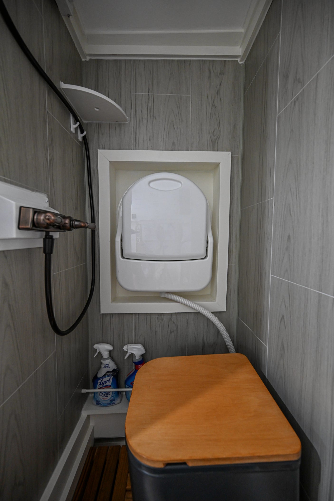 Tiny RV rental bathroom with composting toilet, wall-mounted sink, and shower. Features wood-look tiles and compact design.