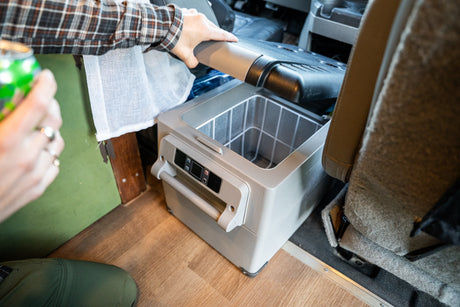 An RV rental user opens a portable fridge inside their camper van, revealing a wire basket. Ideal for road trip drinks.