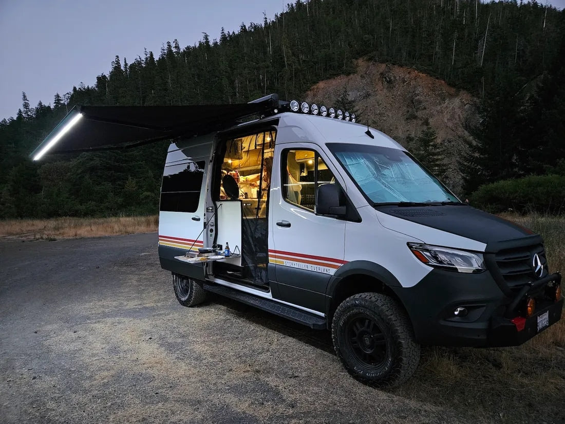 Illuminated Storyteller Overland Sprinter camper van at night. Ideal for your next rv rental adventure, with cozy interior lights and an extended awning.