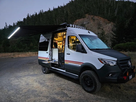 Illuminated Storyteller Overland Sprinter camper van at night. Ideal for your next rv rental adventure, with cozy interior lights and an extended awning.