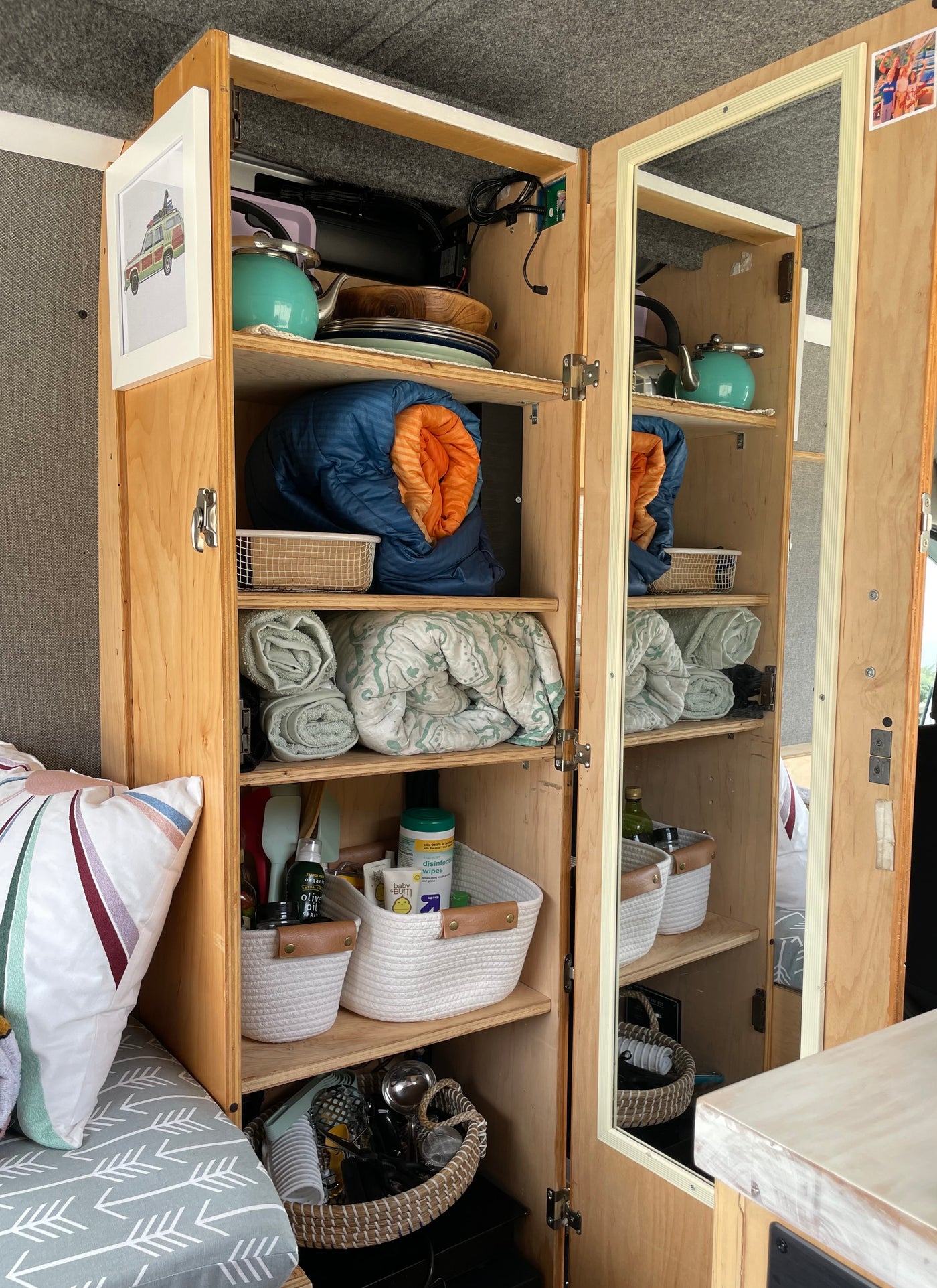 Inside an RV rental: a well-organized wooden cabinet with shelves holding kitchen items, bedding, and supplies. — photo 10