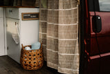 This RV rental interior showcases woven curtains, a "CHASING ALOHA" sign, and a basket with linens, creating a cozy home on wheels.
