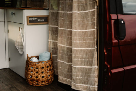 This RV rental interior showcases woven curtains, a "CHASING ALOHA" sign, and a basket with linens, creating a cozy home on wheels.