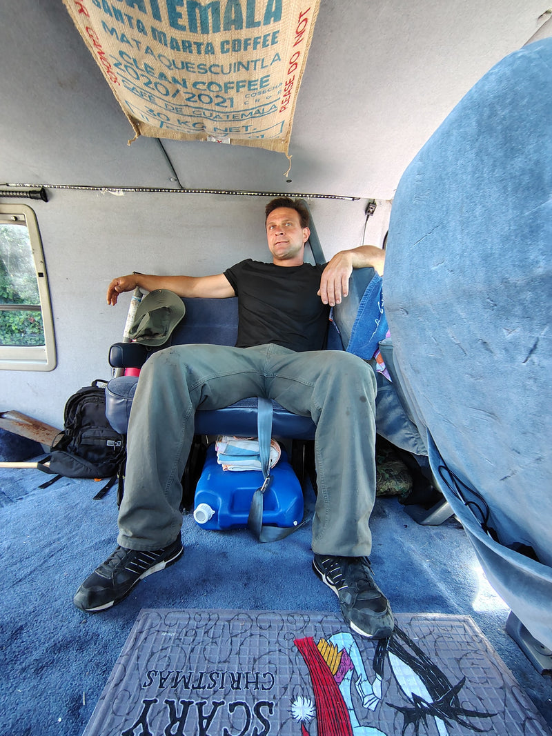 Chilling in an RV rental! A man unwinds in a converted van, with coffee sacks overhead and a 'Scary Christmas' mat. — photo 3
