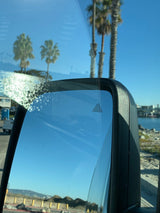 RV rental view: side mirror with blind spot monitor, palm trees & ocean under blue sky.
