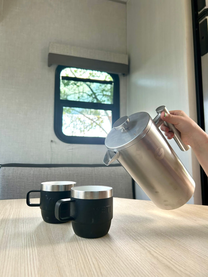 Coffee time in an RV rental! A hand pours from a stainless steel French press into two black YETI mugs on a light wood table. — photo 10