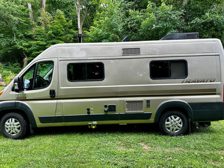  a comfortable rv rental option parked on green grass. Ideal for travel.|RV rental: Tan Ram ProMaster Travato camper van parked on green grass in a wooded area
