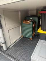 Spacious RV rental storage compartment with two green suitcases, a ladder, and storage bins on a diamond plate floor, ready for travel.