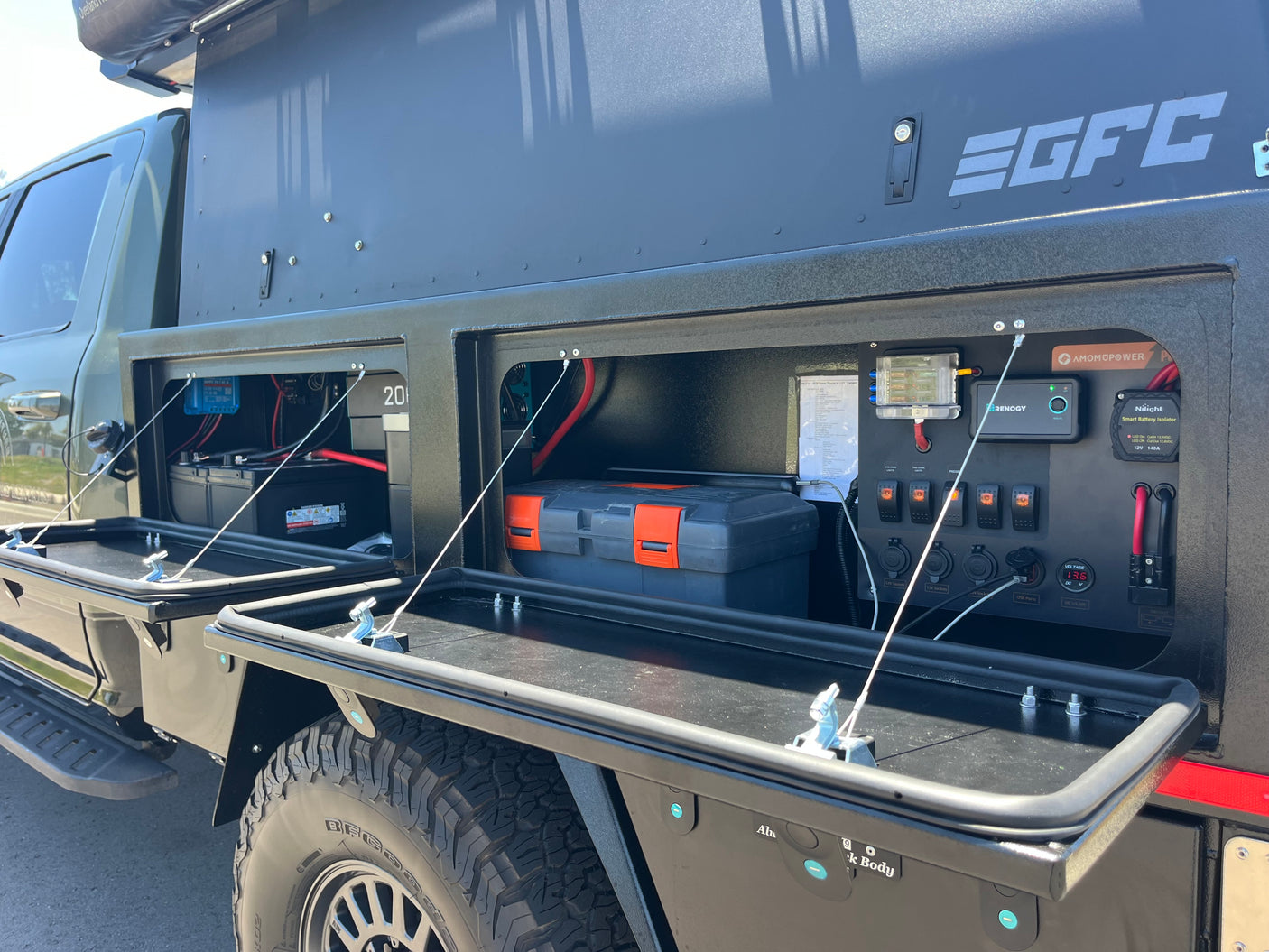 An RV rental truck's open side compartments reveal a sophisticated off-grid power system with batteries, Renogy, and charging ports.